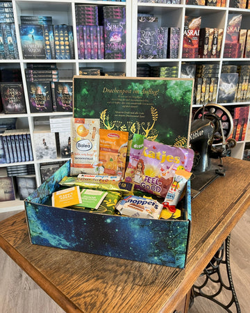 Das Produktbild zeigt vorn eine geöffnete Drachenpost in blauem Schuppen-Design. Man sieht den in den Boxdeckel geklebten Brief zum Thema #mytime und in der Box zum Thema passende Goodies - Süßigkeiten und andere Kleinigkeiten. Im Hintergrund sieht man die Bücherregale des Verlagsladens.